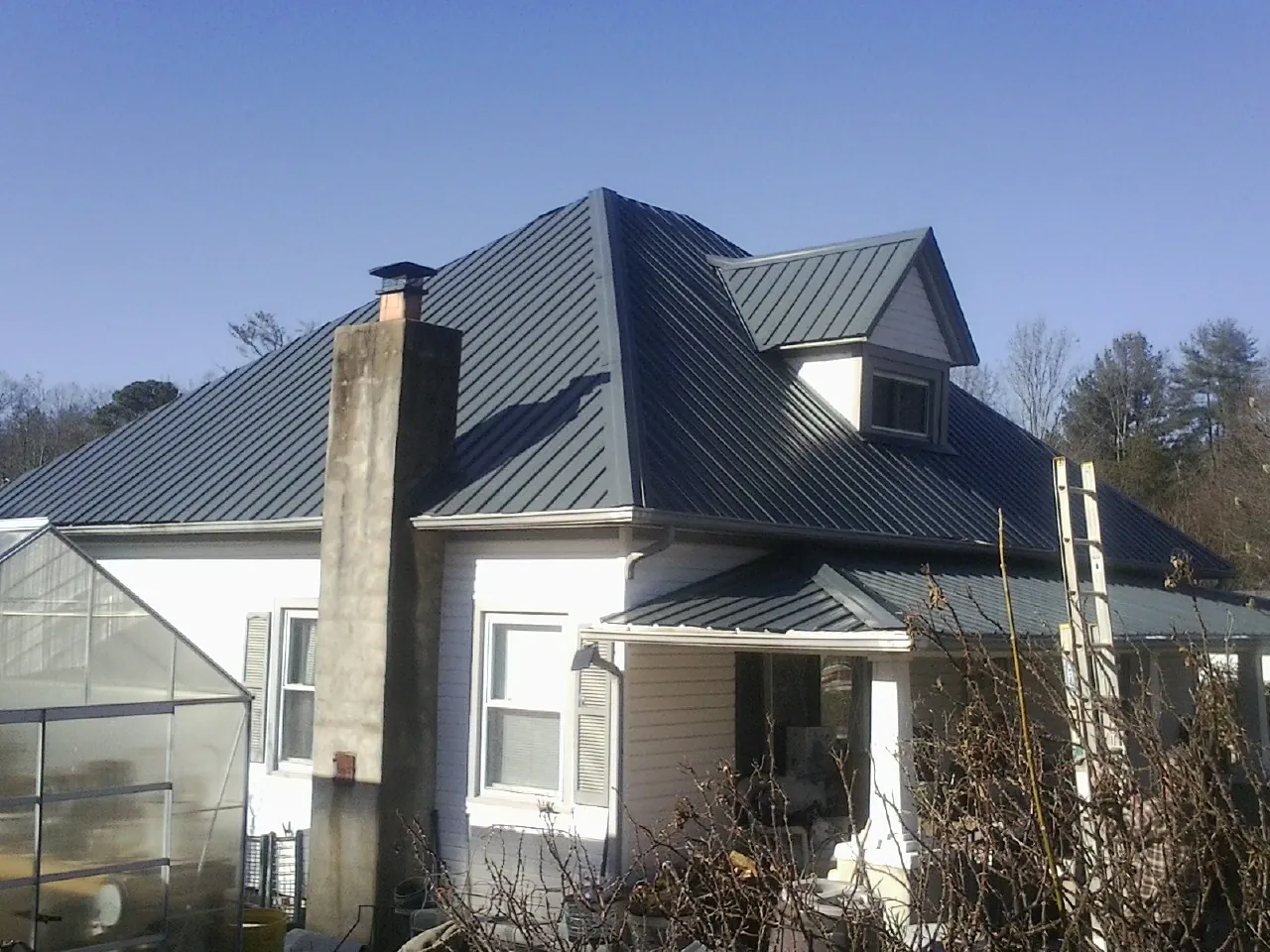 Dark blue standing seam metal roof on a white farmhouse with dormer — Slate & Tile Roof Repair by Roofing Brothers in Wasco