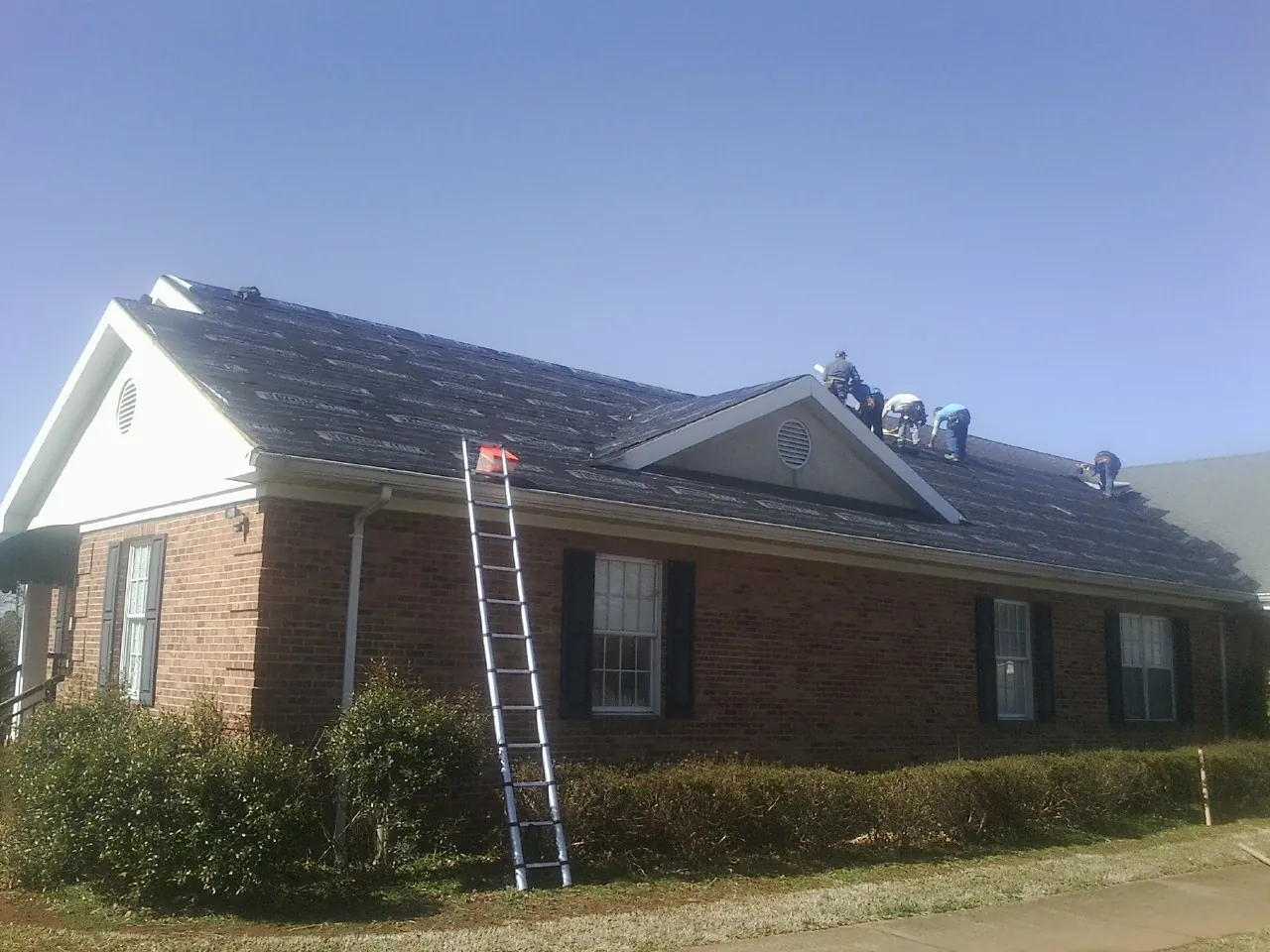 Crew tearing shingles off a brick ranch roof with a ladder set — Metal Roof Repair work by our crew in Wasco
