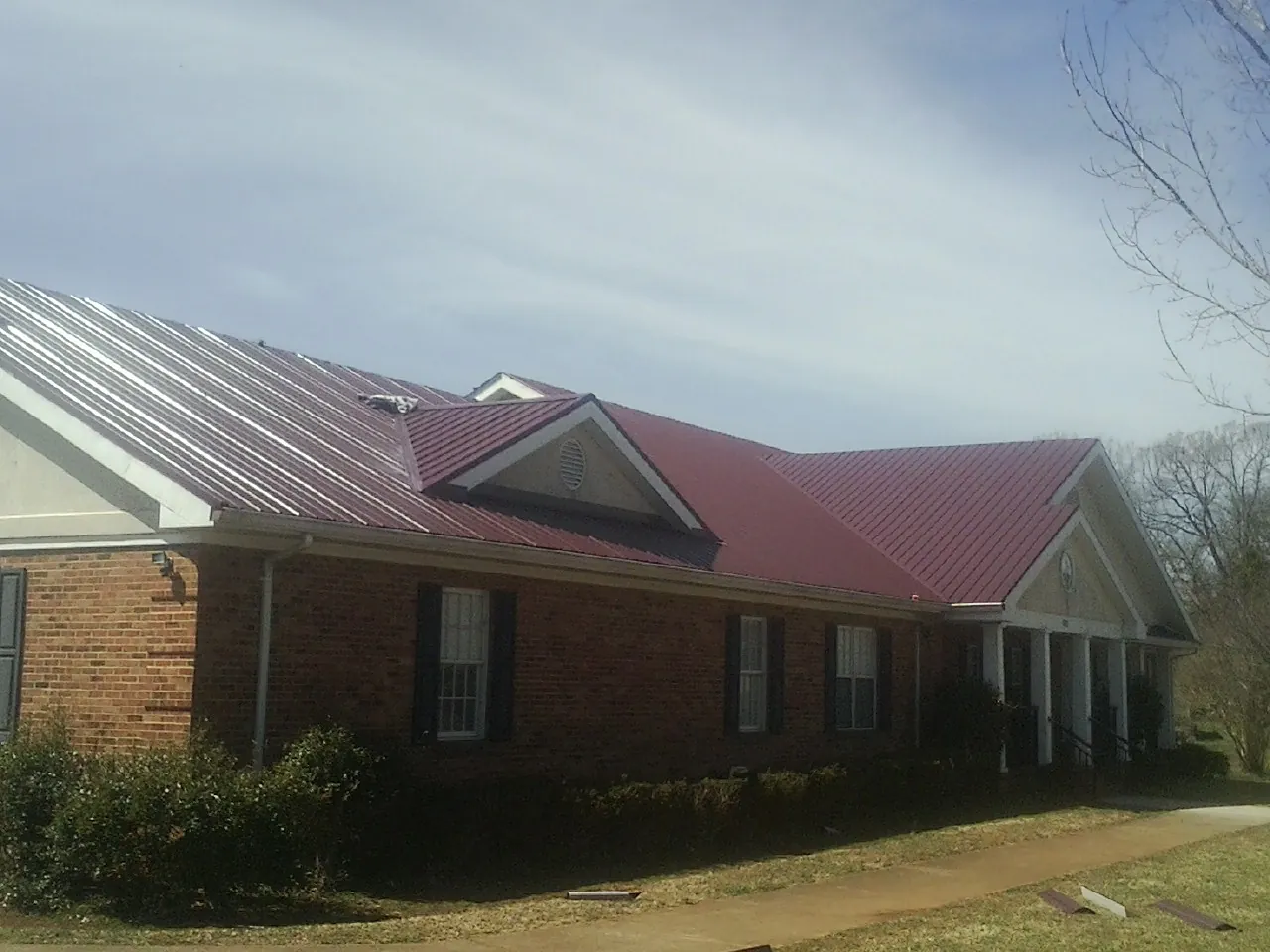 Red metal roof with gabled entries on a long brick building, from a Hail Damage Roof Repair job in Wasco