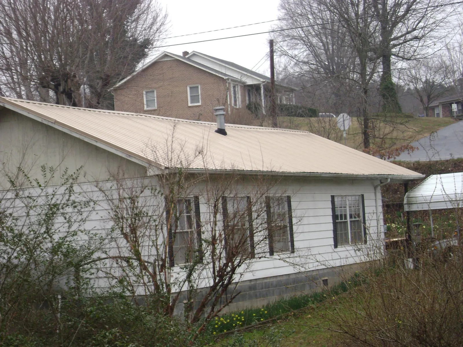 Tan metal roof on a white sided house set into a hillside — Commercial Roofing by Roofing Brothers in Wasco